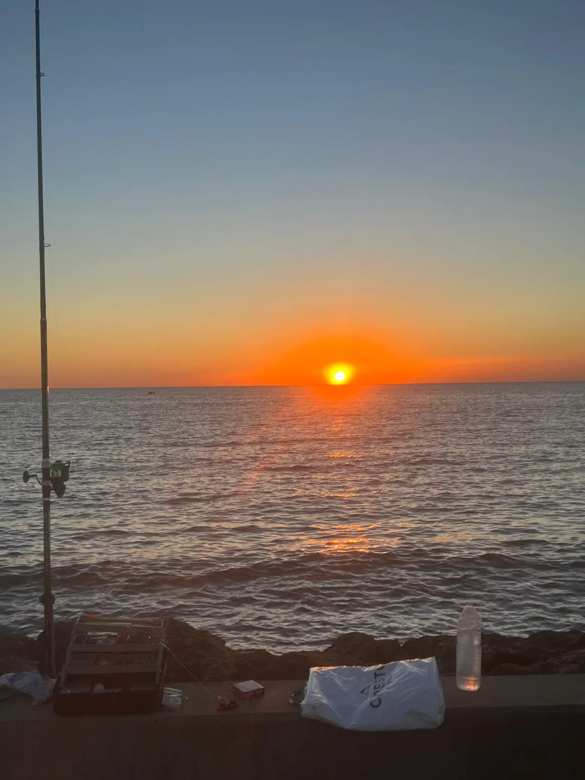 Une canne à pêche dressée face à la mer au coucher du soleil