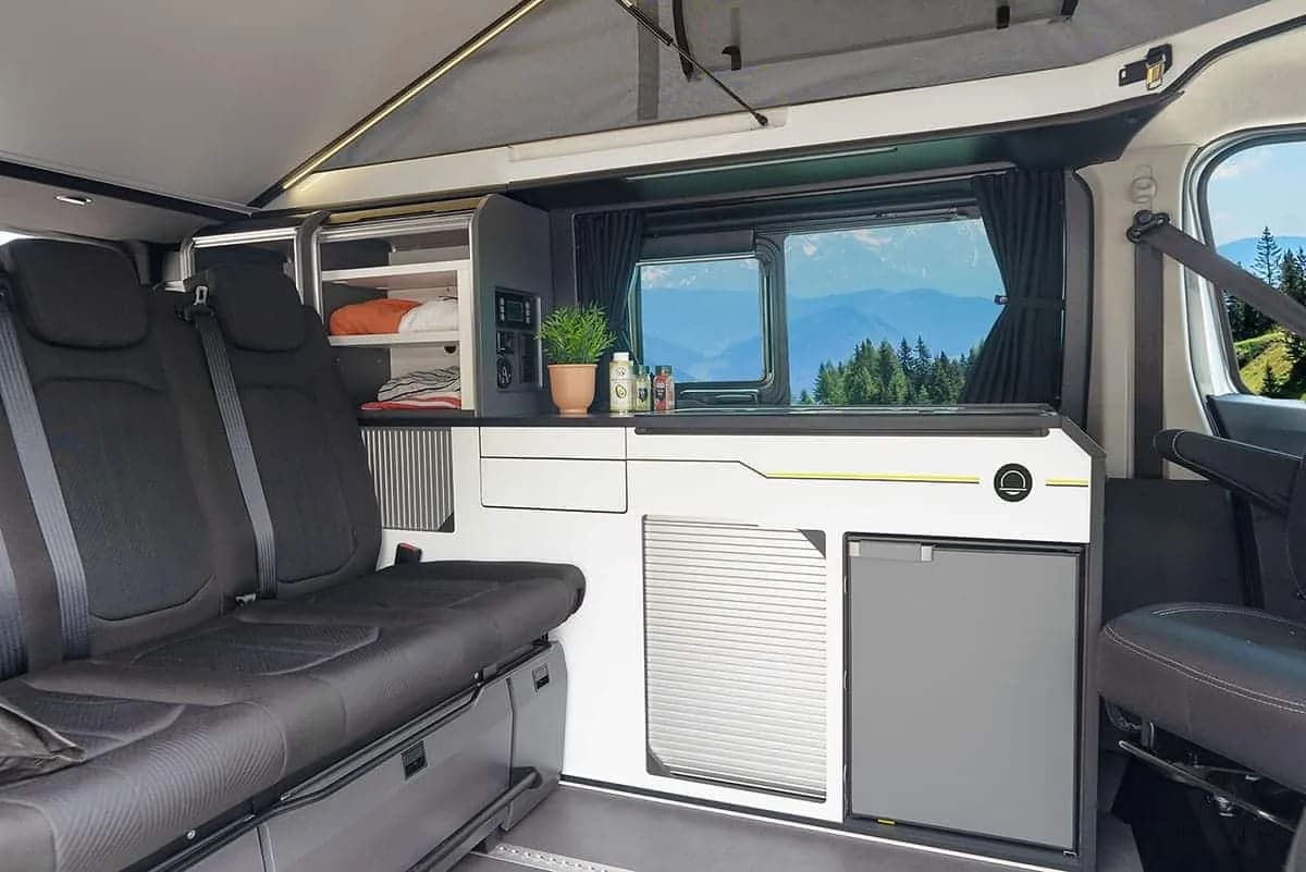 La banquette trois places, le meuble cuisine avec réfrigérateur et les rangements, fenêtre ouverte sur la montagne