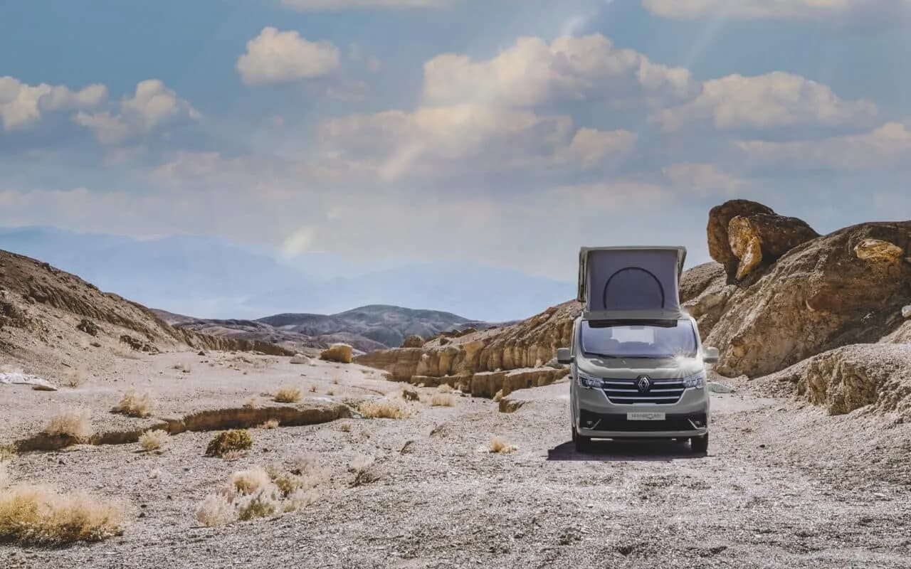 Le van toit relevé sur une piste entre des rochers, sous un grand ciel nuageux