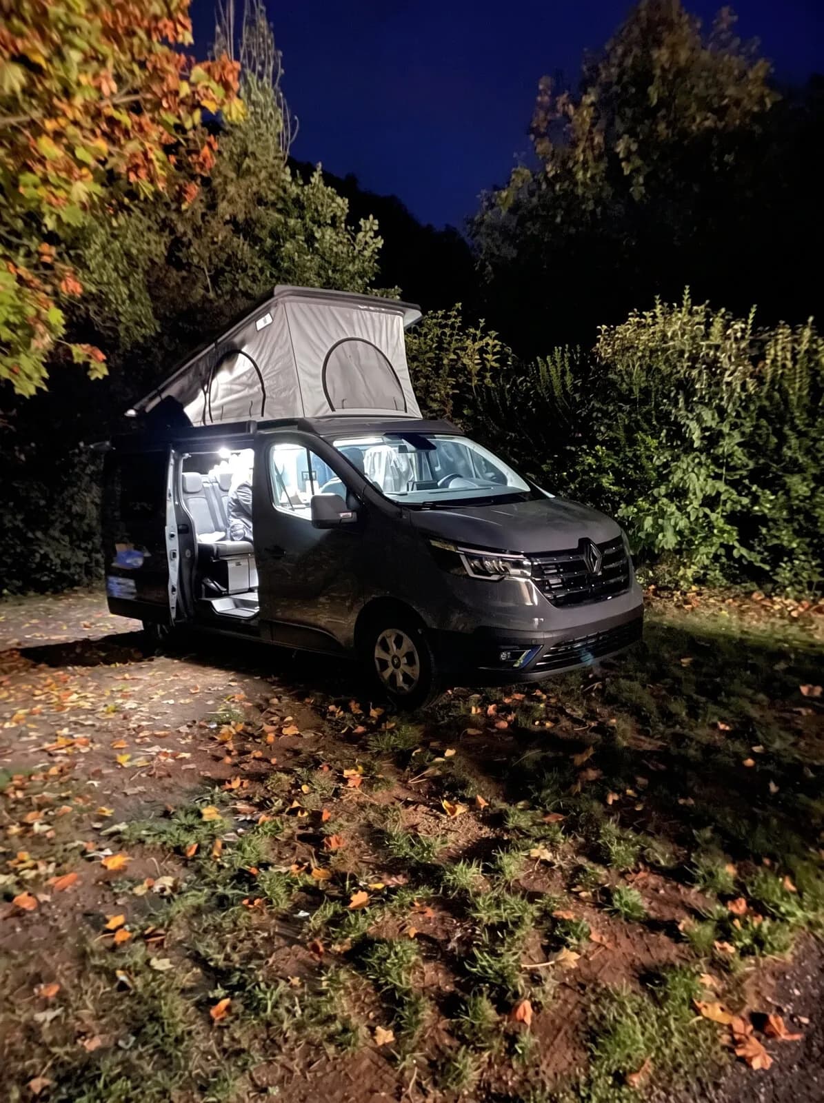 Le van garé de nuit sous les arbres, toit relevé et intérieur éclairé