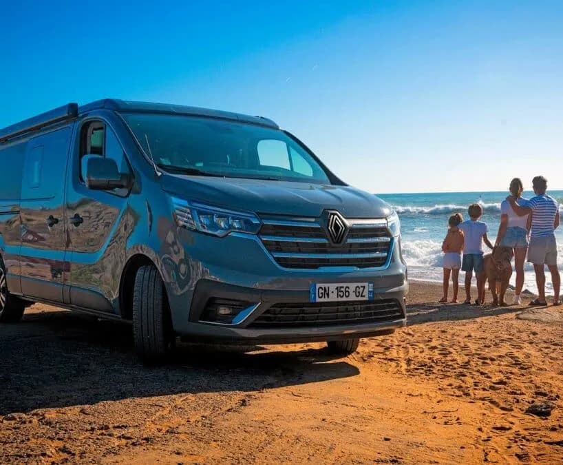 Le van Renault Trafic gris garé sur le sable, une famille et son chien face aux vagues
