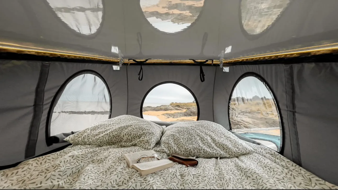 Le lit double sous le toit relevable, avec ses fenêtres rondes en toile ouvertes sur une plage